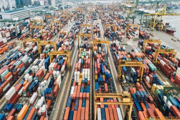 A large number of shipping containers in a busy cargo port. Original public domain image from Wikimedia Commons